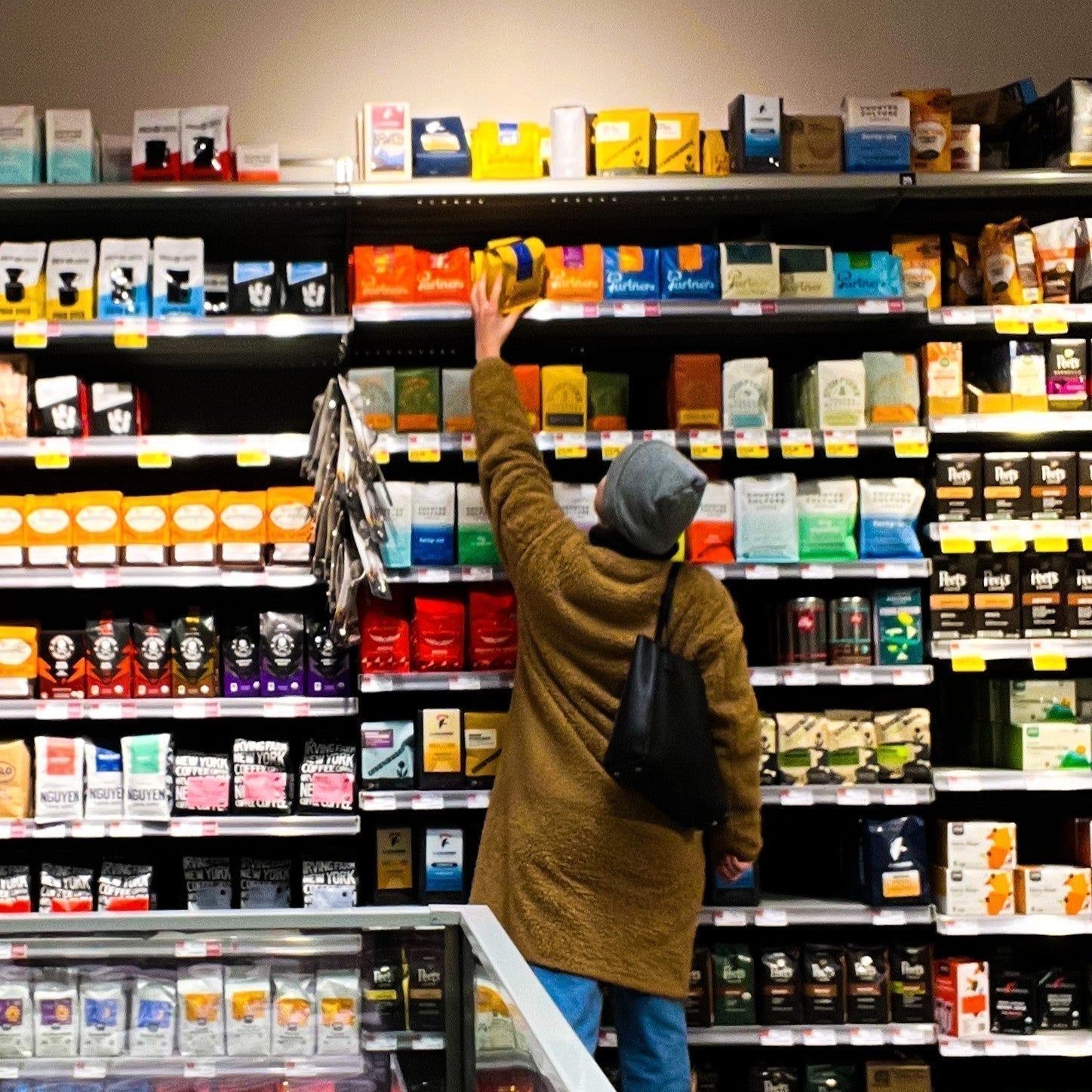 Partners Coffee Recent Features blog post. This image displays a customer reaching up towards a bag of Partners Coffee on the shelves of a Whole Foods store